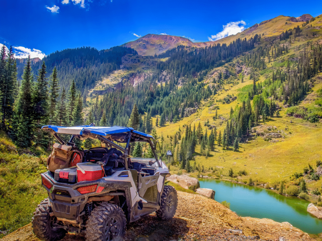 An SXS rental on a rugged off-road trail with a scenic lake in the background