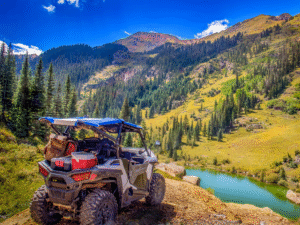 An SXS rental on a rugged off-road trail with a scenic lake in the background
